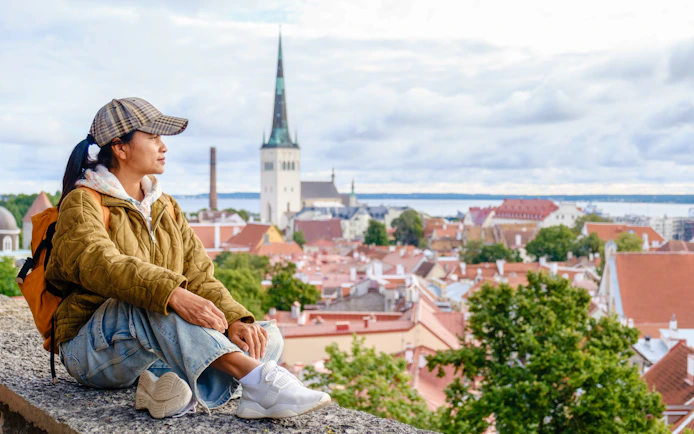 Traveler sitting at Kohtuotsa viewpoint overlooking Tallinn's old town, Estonia.