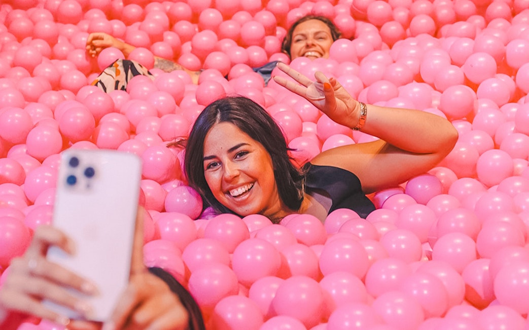 Visitors enjoying a ball pit at Pink Palace, taking a selfie.