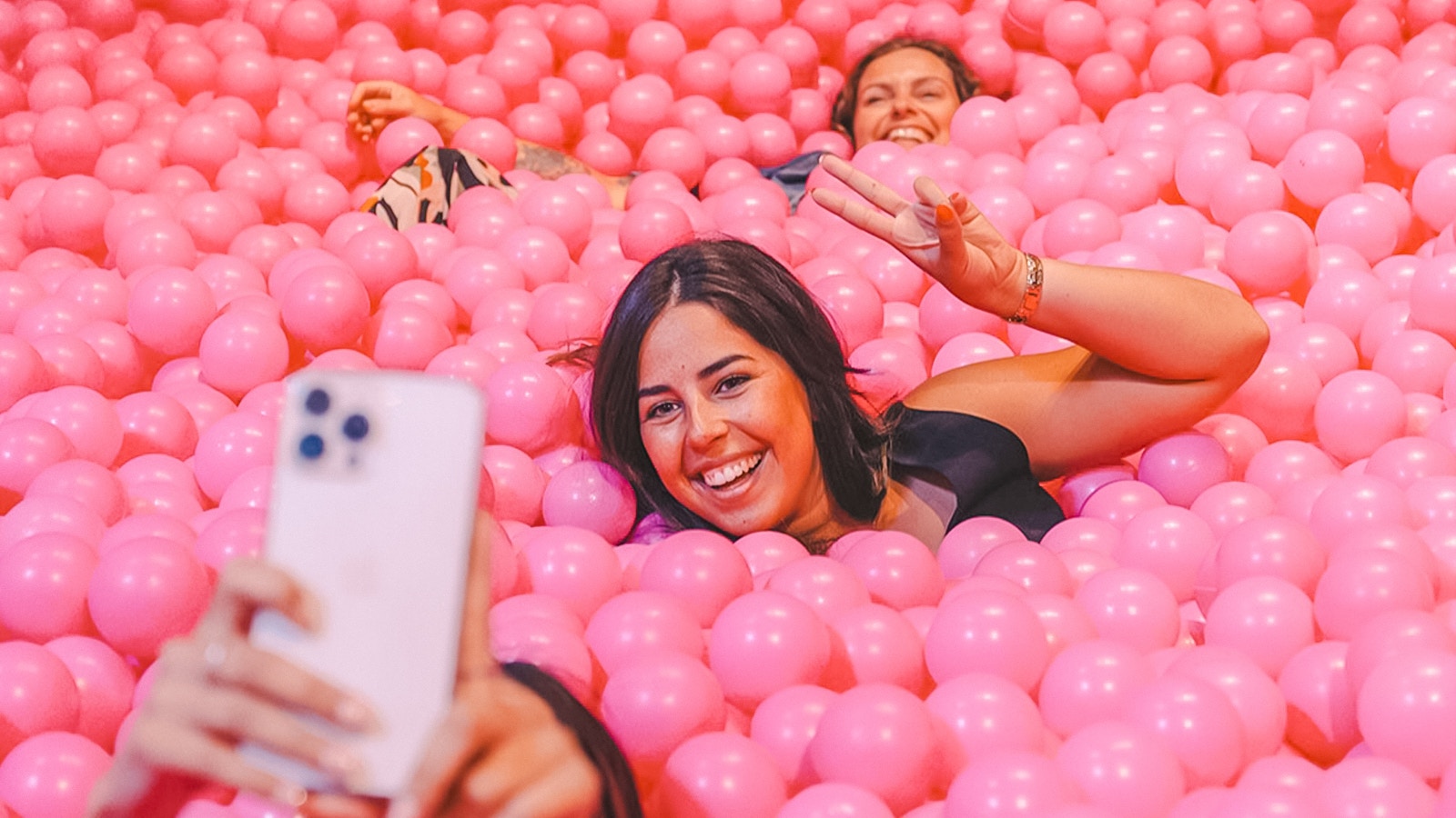 Visitors enjoying a ball pit at Pink Palace, taking a selfie.