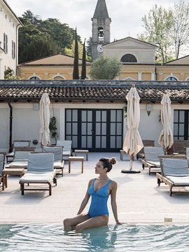 Woman relaxing by the pool at QC Terme Garda, Italy, with historic architecture in the background.