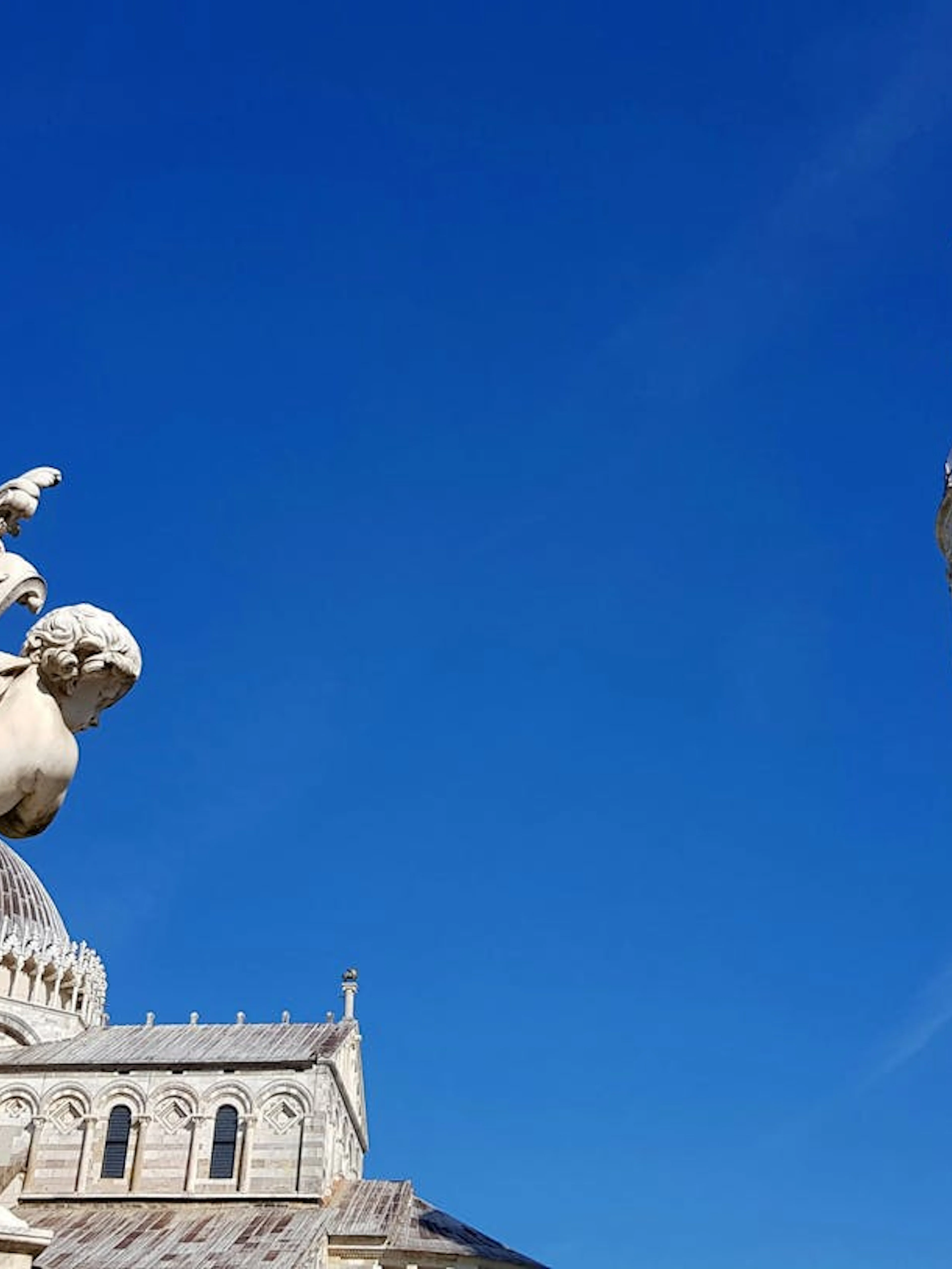 Leaning Tower of Pisa and cherub statue under clear blue sky.