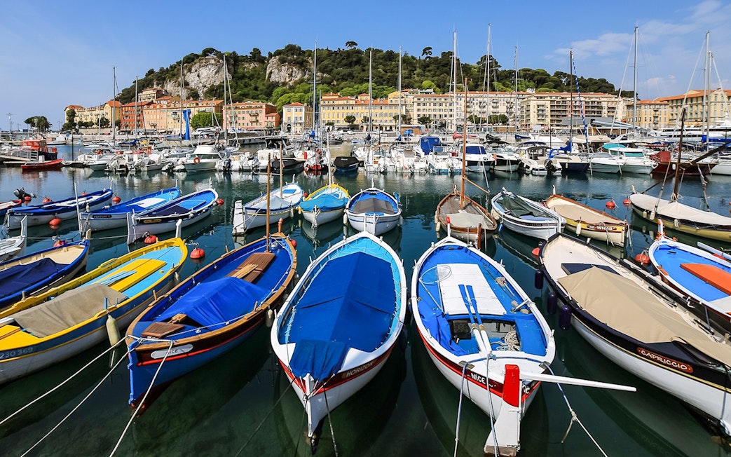 Colorful boats docked at Nice harbor with hillside buildings in the background.