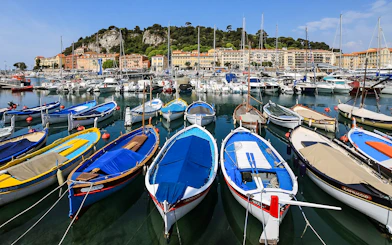 Colorful boats docked at Nice harbor with hillside buildings in the background.