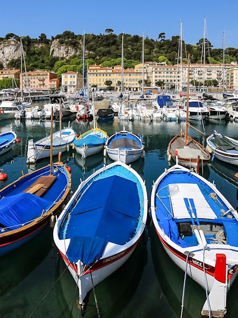 Colorful boats docked at Nice harbor with hillside buildings in the background.