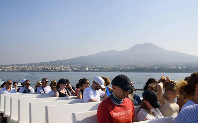 Tourists on a boat with Mount Vesuvius in the background during an Amalfi Coast cruise.