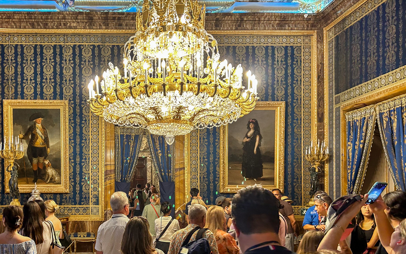Royal Palace of Madrid tour group under ornate chandelier in opulent room.