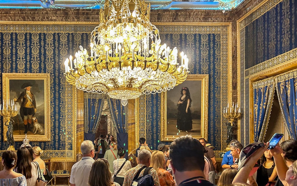 Royal Palace of Madrid tour group under ornate chandelier in opulent room.