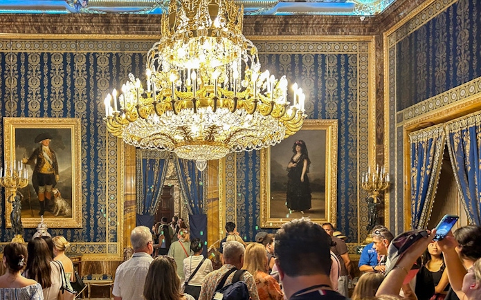 Royal Palace of Madrid tour group under ornate chandelier in opulent room.