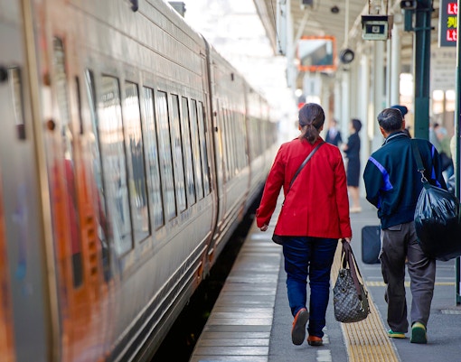 Couple waiting at a train station in Japan with traditional architecture in the background.