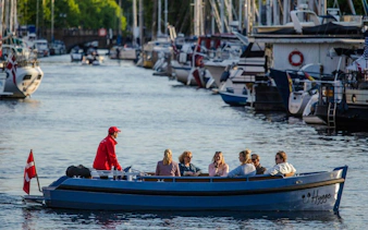 Guests on a guided boat tour in Copenhagen canal with Danish flag and moored boats.