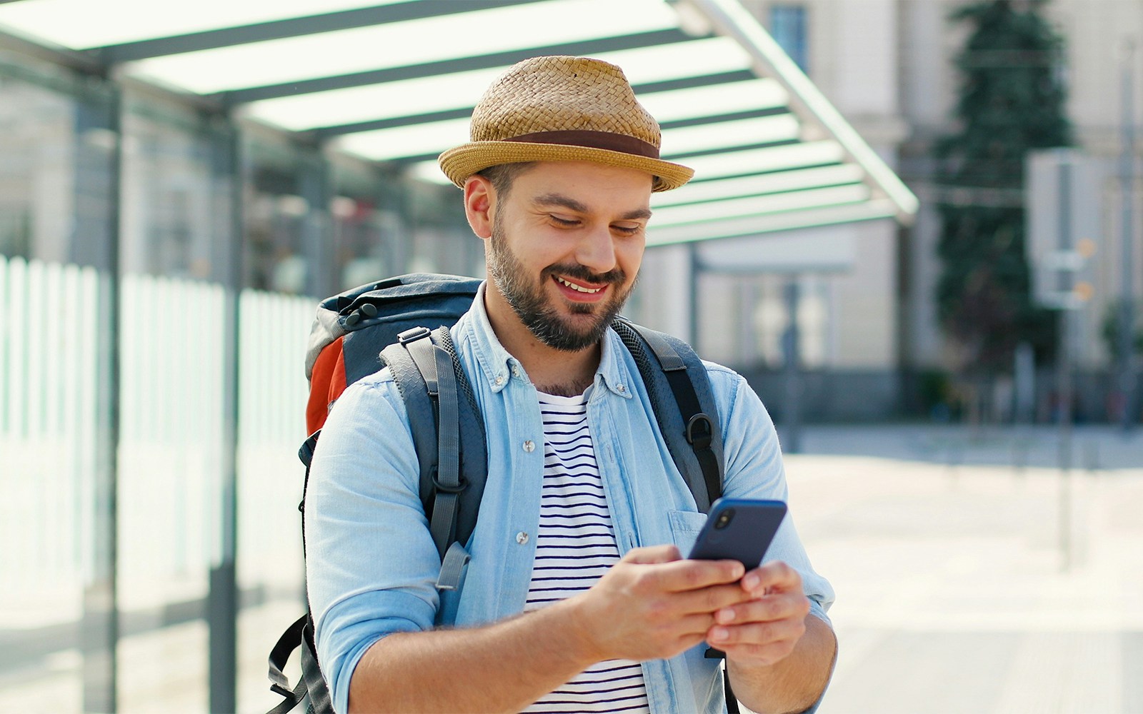 Man with backpack using phone at a bus stop.