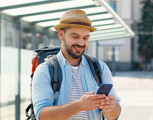 Man with backpack using phone at a bus stop.
