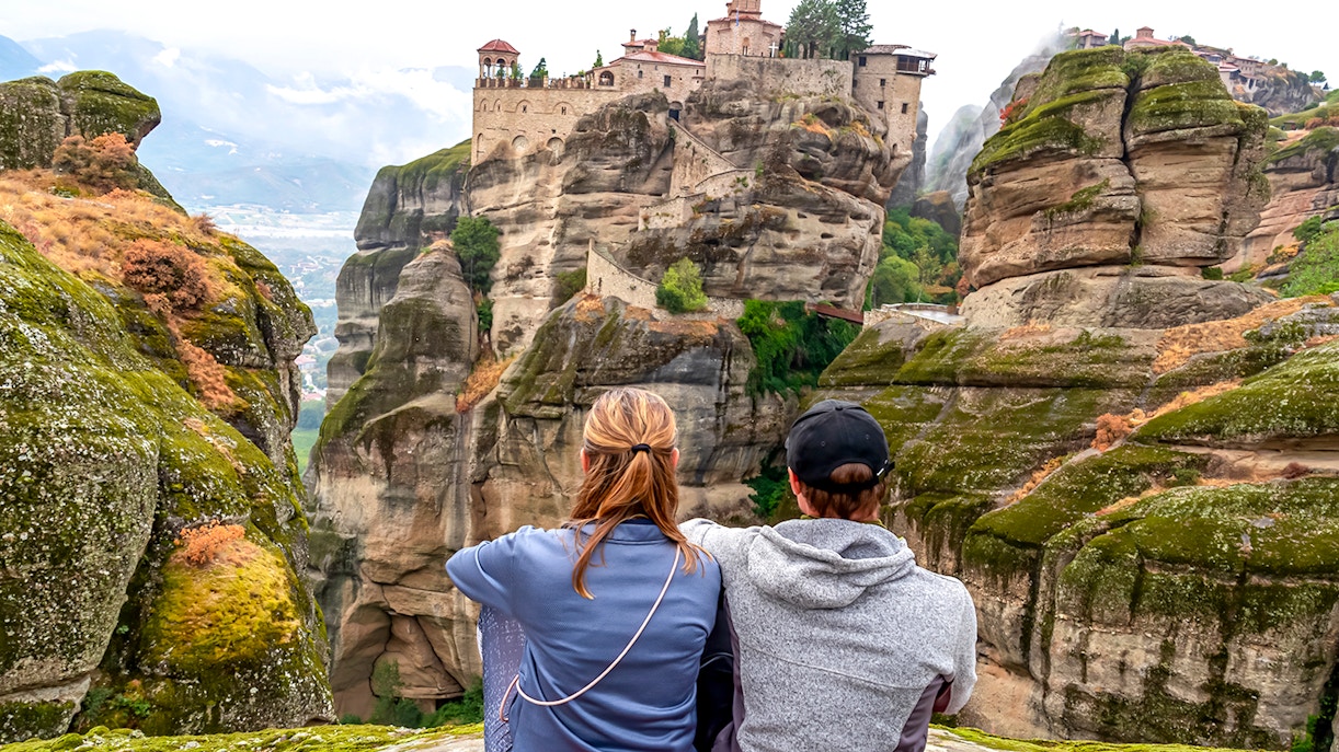 Two people sitting and viewing the Meteora Monasteries on rock formations in Thessaloniki, Greece.