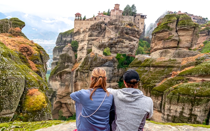 Two people sitting and viewing the Meteora Monasteries on rock formations in Thessaloniki, Greece.