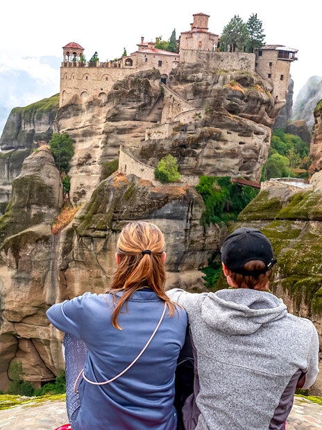 Two people sitting and viewing the Meteora Monasteries on rock formations in Thessaloniki, Greece.
