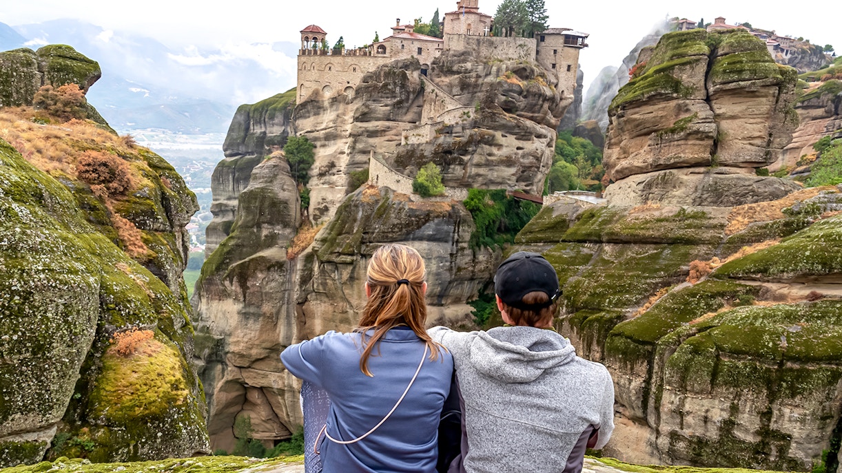 Two people sitting and viewing the Meteora Monasteries on rock formations in Thessaloniki, Greece.