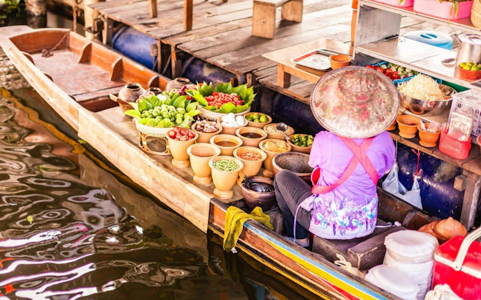 Vendor selling fresh produce from a boat at Damnoen Saduak Floating Market, Thailand.