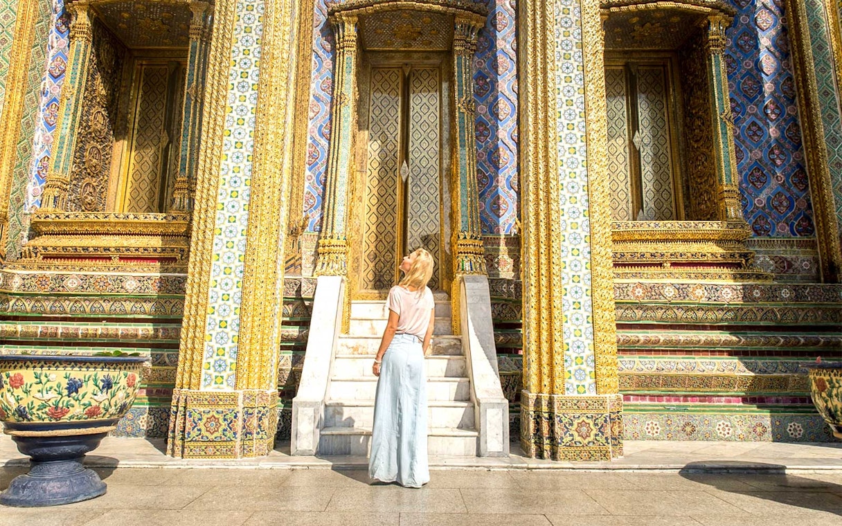 Visitor admiring ornate entrance of Grand Palace temple in Bangkok.