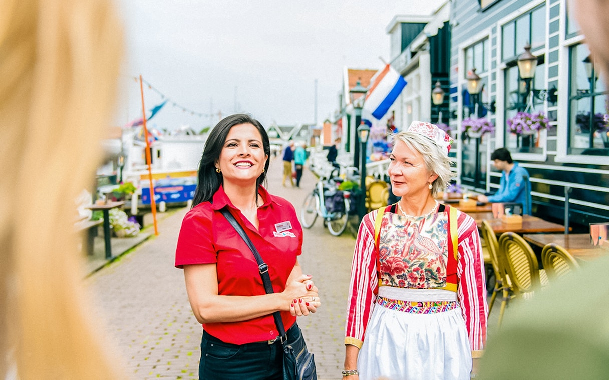 Guide leading a tour in Volendam with traditional Dutch attire in the background.