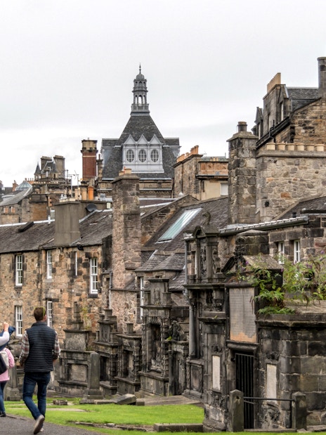 Tourists walking through historic Edinburgh on a Harry Potter tour, passing stone buildings.