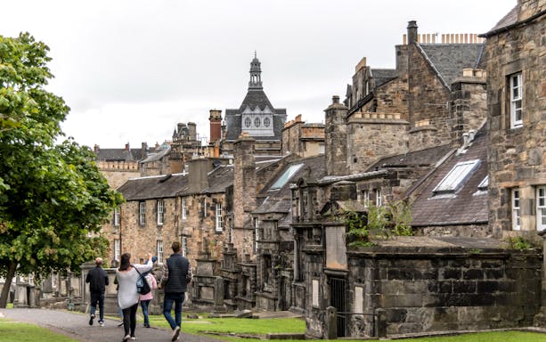 Tourists walking through historic Edinburgh on a Harry Potter tour, passing stone buildings.