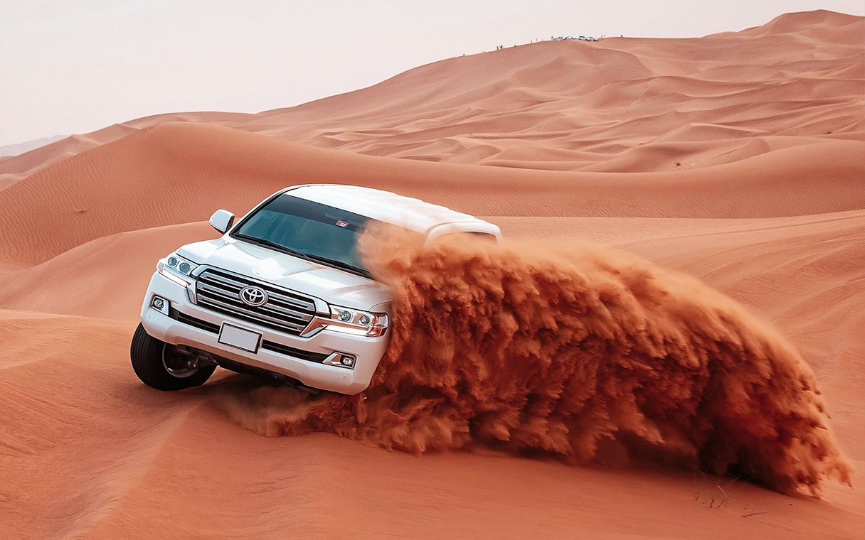 SUV driving through red desert dunes during Evening Red Dune Desert Safari.