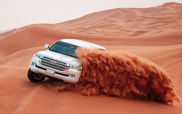 SUV driving through red desert dunes during Evening Red Dune Desert Safari.