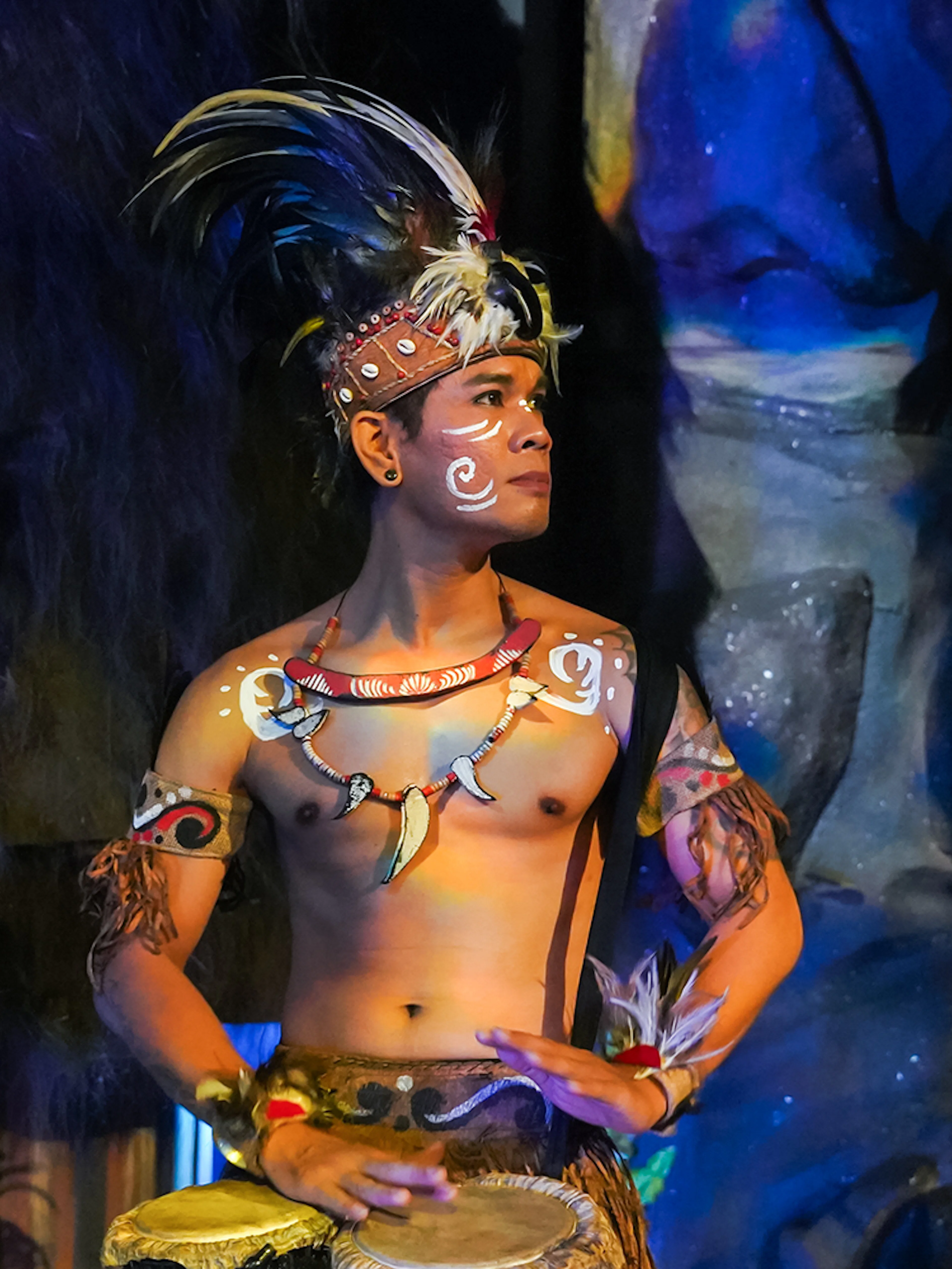 Performer in traditional Indonesian attire playing drums at the Devdan Show, Bali.