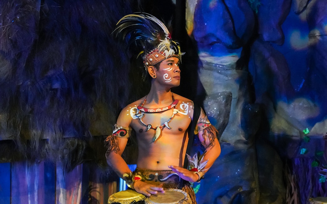 Performer in traditional Indonesian attire playing drums at the Devdan Show, Bali.