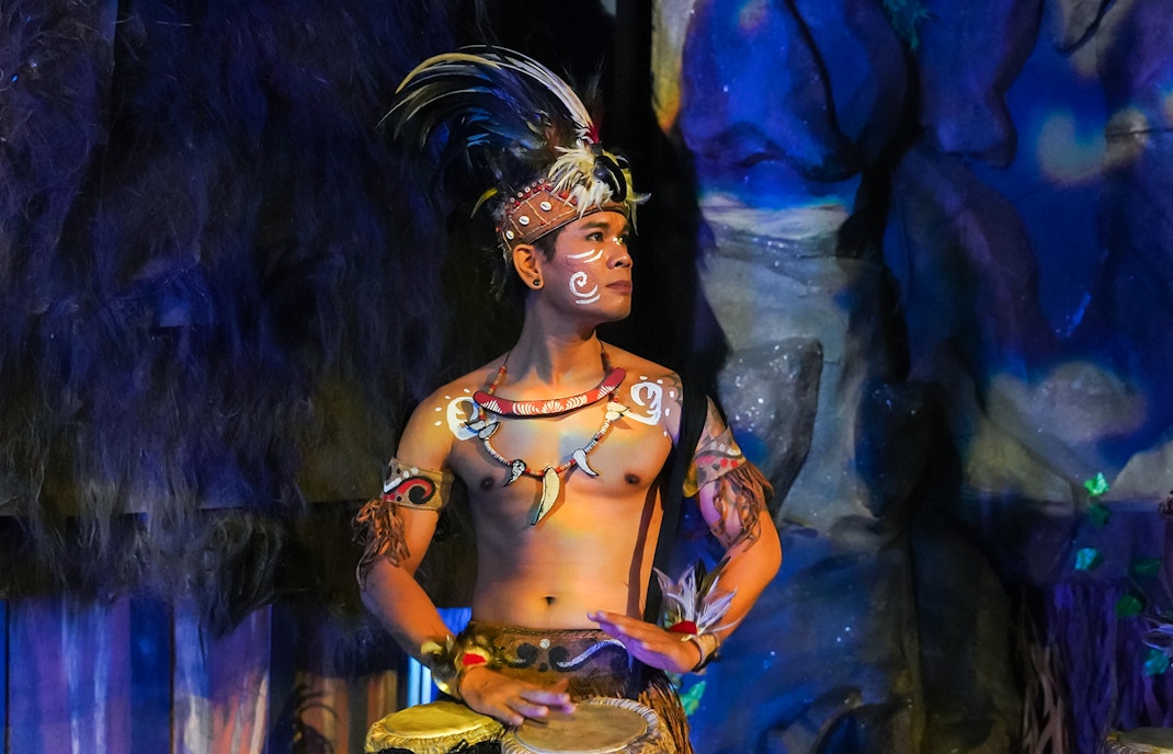 Performer in traditional Indonesian attire playing drums at the Devdan Show, Bali.