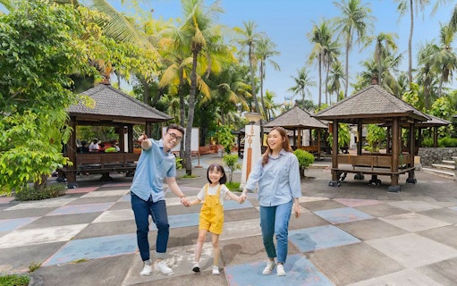 Family enjoying Ancol Atlantis Water Adventure Park with tropical huts and palm trees.