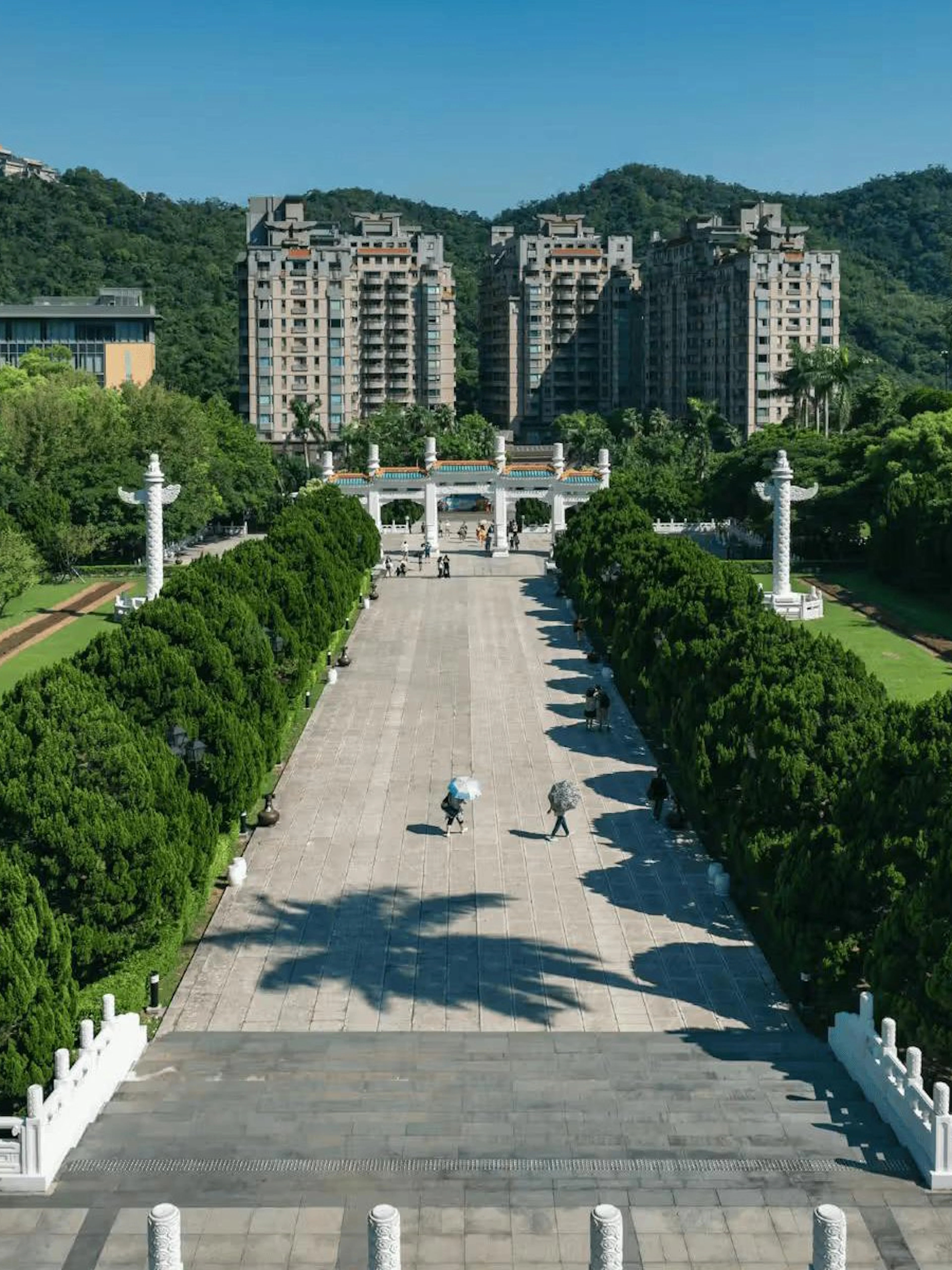 Pathway leading to the National Palace Museum entrance, Taipei, with lush greenery and distant buildings.