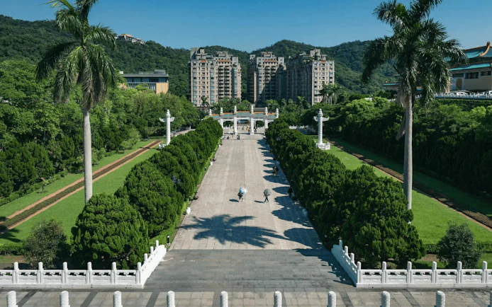 Pathway leading to the National Palace Museum entrance, Taipei, with lush greenery and distant buildings.