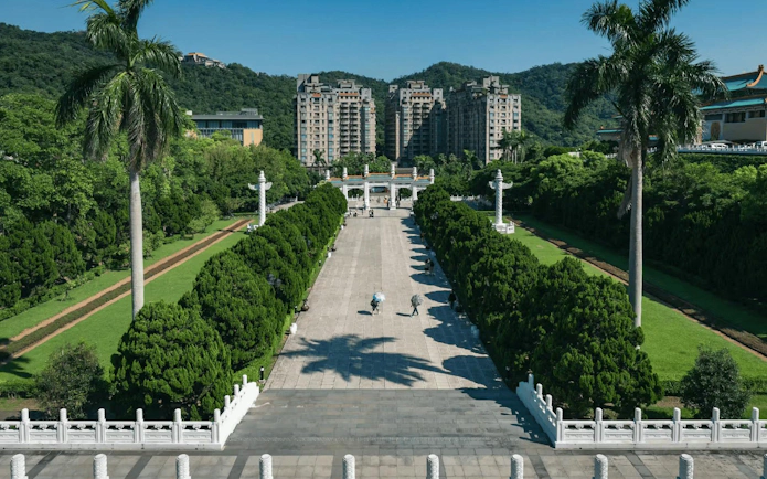 Pathway leading to the National Palace Museum entrance, Taipei, with lush greenery and distant buildings.