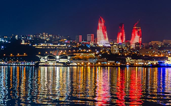 Baku skyline with illuminated Flame Towers reflecting on Caspian Sea during boat tour.