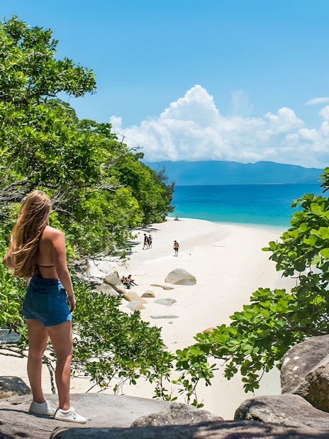 Tourists walking along a sandy beach on Fitzroy Island, surrounded by lush greenery and ocean views.