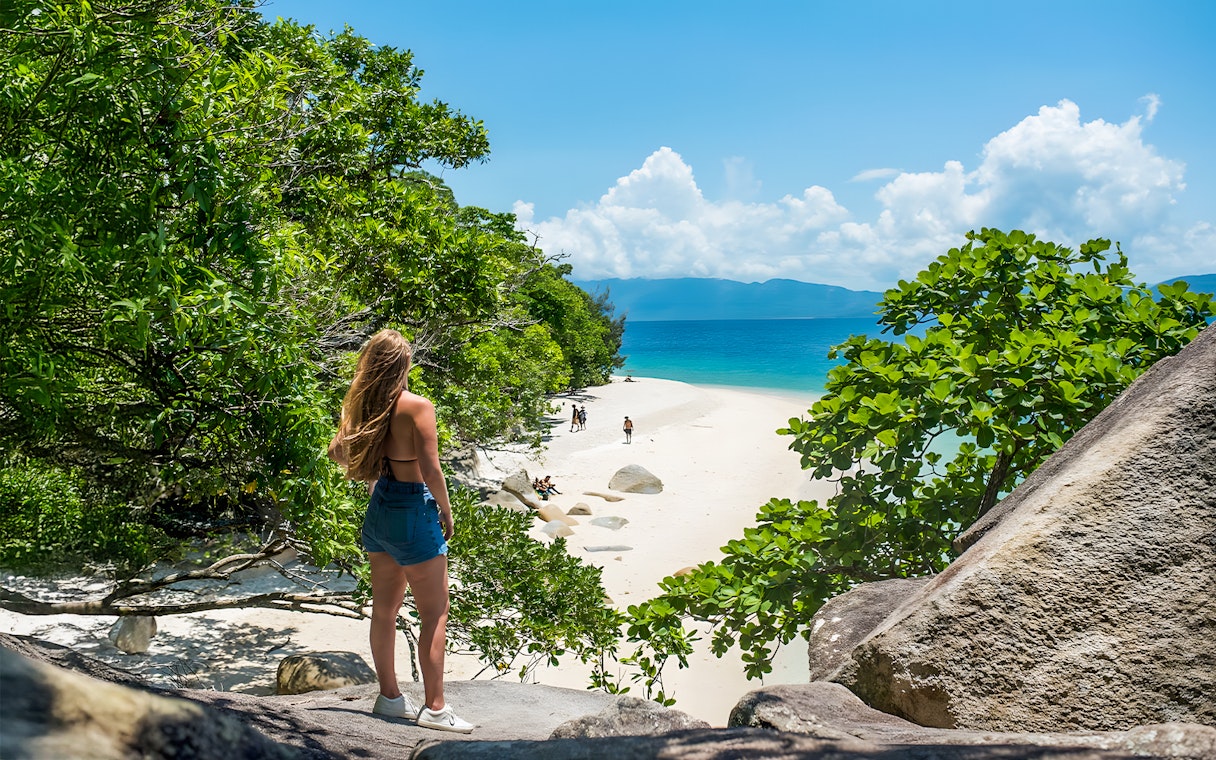 Tourists walking along a sandy beach on Fitzroy Island, surrounded by lush greenery and ocean views.