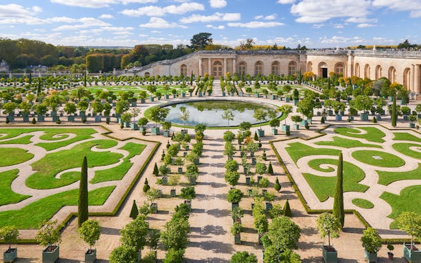 Palace of Versailles gardens with manicured hedges and central fountain.