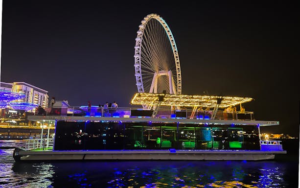 Houseboat with lights on water near Ain Dubai Ferris wheel at night.