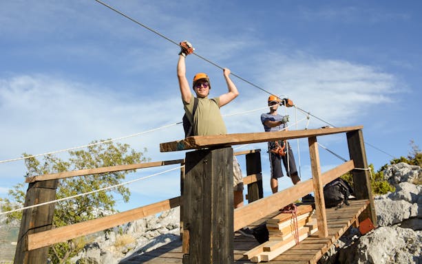 Two people preparing for a zipline adventure in Split, Croatia, on a wooden platform.