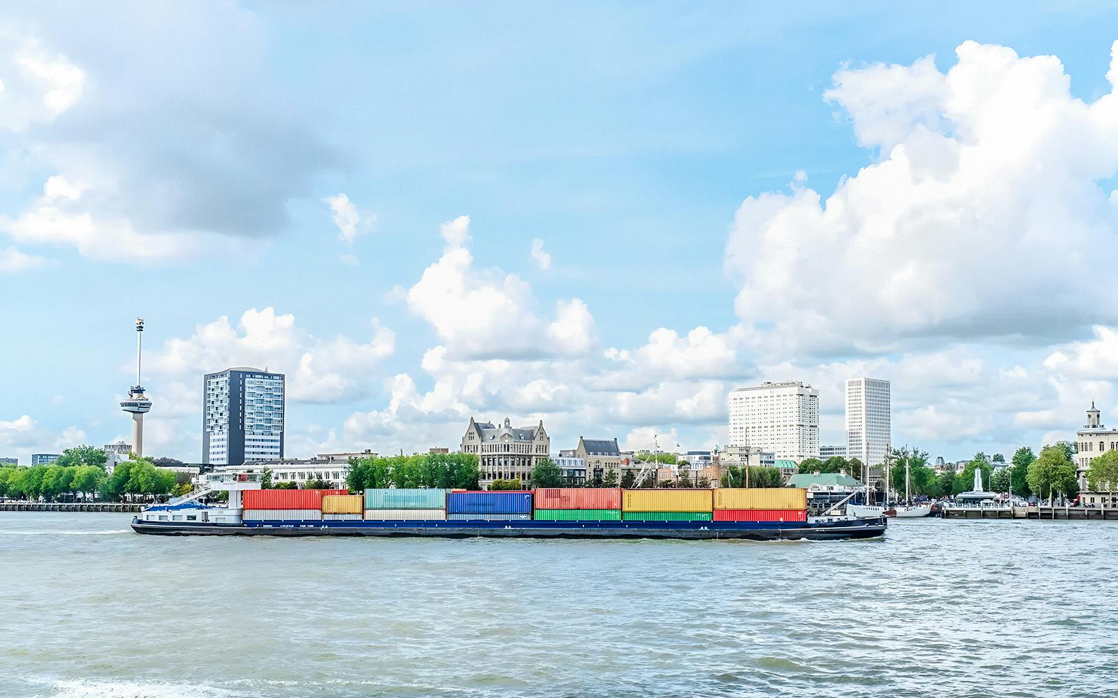 Container ship on Rotterdam harbor with city skyline in the background.