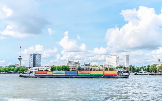 Container ship on Rotterdam harbor with city skyline in the background.