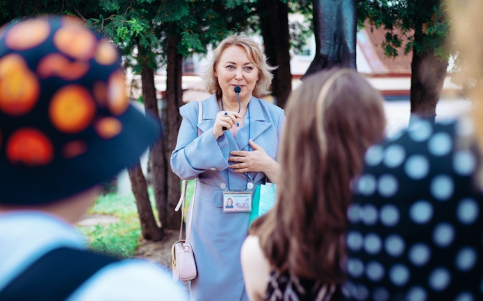 Tour guide speaking to a group outdoors with trees in the background.