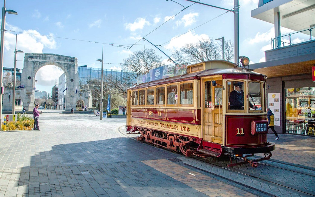 Christchurch tram passing near Bridge of Remembrance on a sunny day.