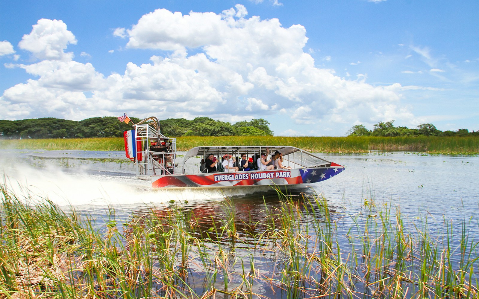 Airboat gliding through Everglades with tourists, showcasing Everglades Holiday Park tour.