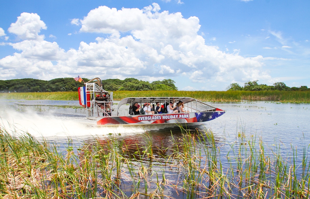 Airboat gliding through Everglades with tourists, showcasing Everglades Holiday Park tour.