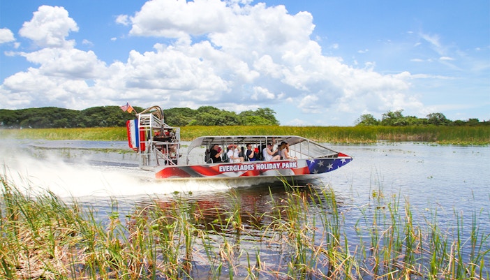 Airboat gliding through Everglades with tourists, showcasing Everglades Holiday Park tour.