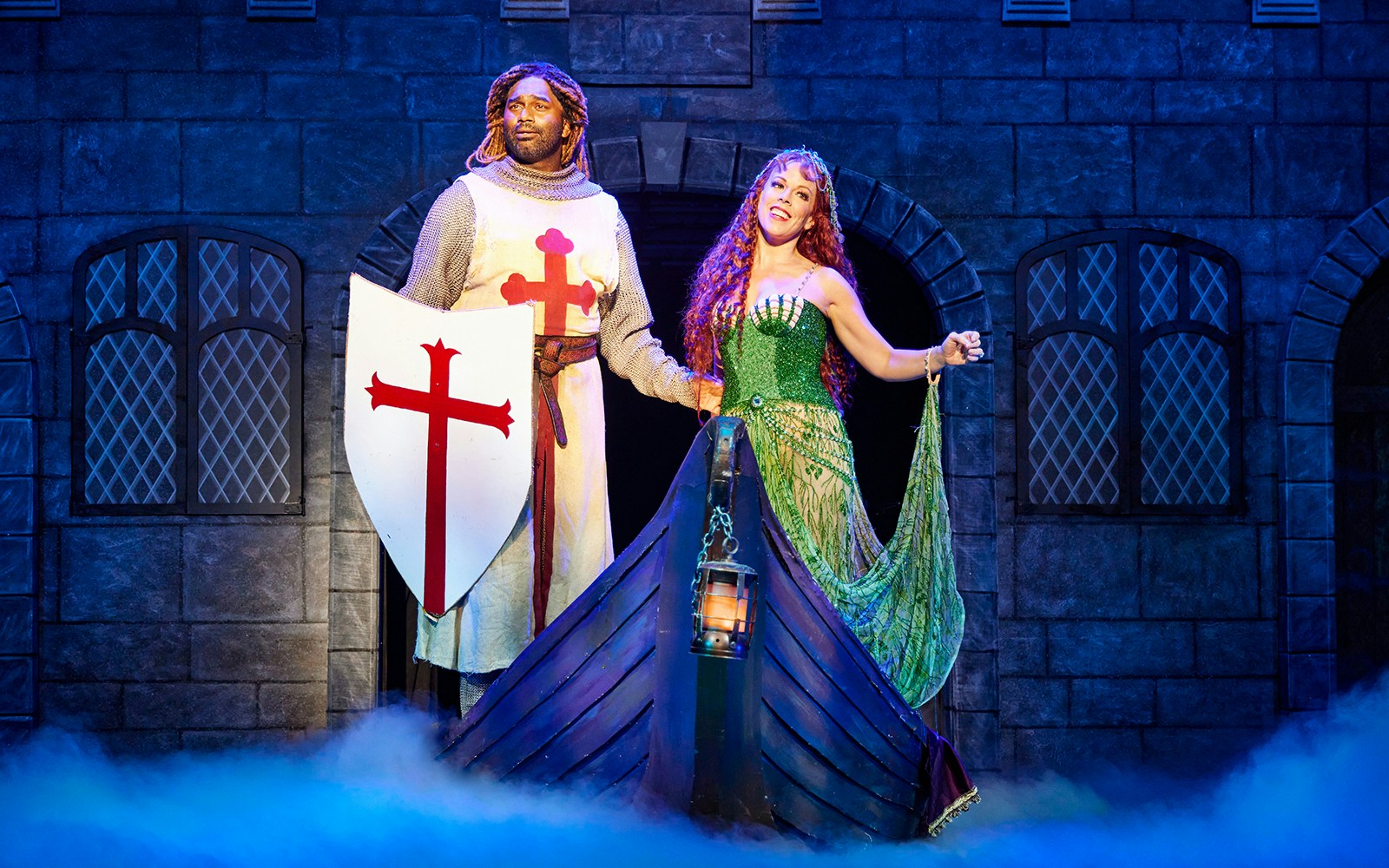 Knight and woman in medieval attire on stage during Spamalot performance.