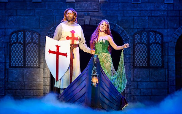 Knight and woman in medieval attire on stage during Spamalot performance.