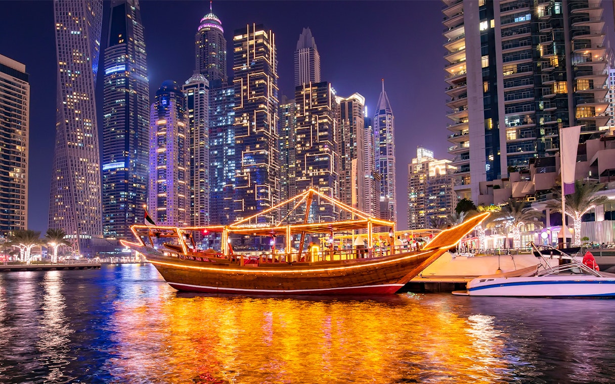 Traditional dhow boat illuminated at night in Dubai Marina with skyscrapers in the background.